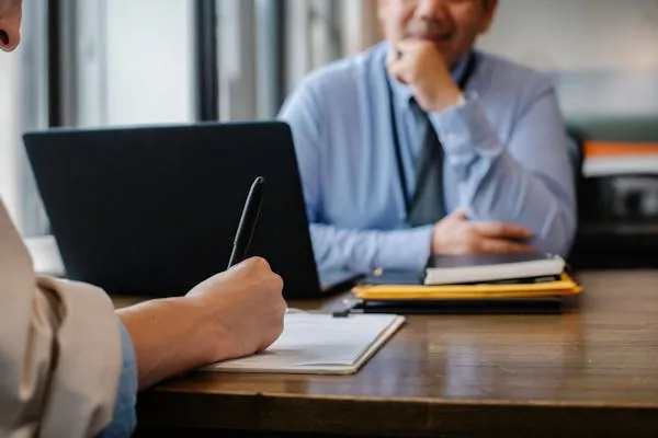 A client meeting across a desk, one person taking notes
